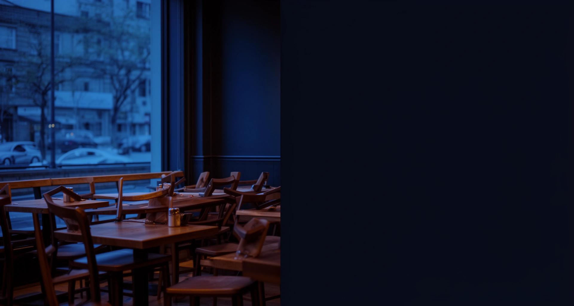Salón de un restaurante vacío a la hora azul, con las sillas sobre las mesas y luz de la calle entrando por el ventanal